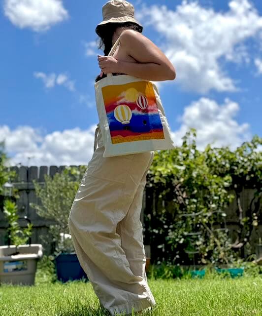 Hand-painted hot air balloon tote bag being carried in a garden